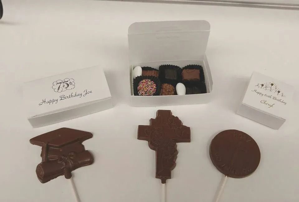 Chocolate treats, including boxed chocolates and lollipops shaped like a graduation cap, cross, and circle.