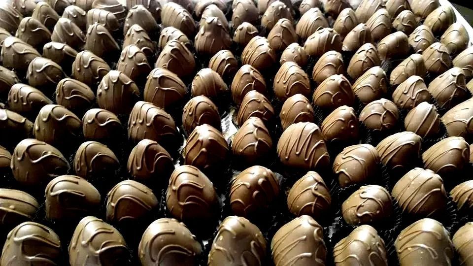 Close-up of rows of chocolate-covered strawberries, drizzled with white chocolate, on a dark surface.