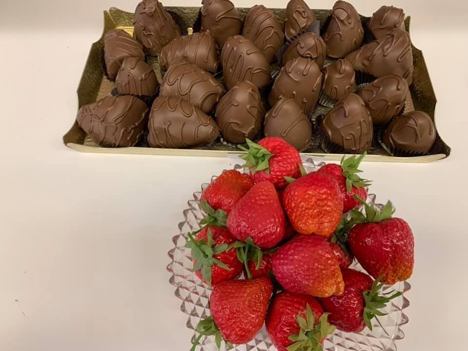 Chocolate-covered treats on a tray, strawberries in a glass dish on a white surface.