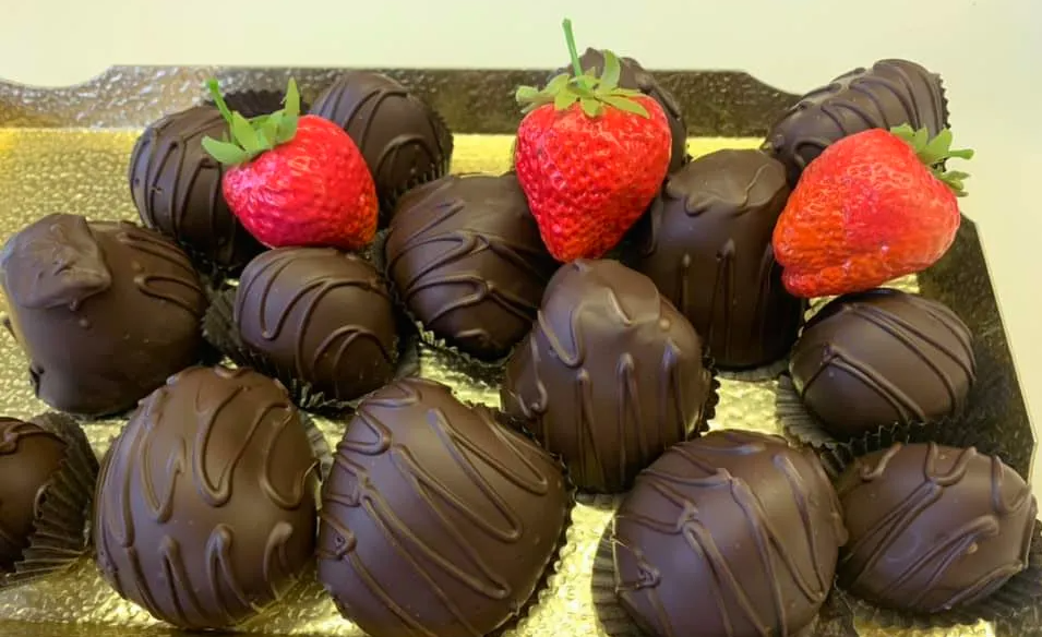 Chocolate-covered strawberries on a golden tray. Dark chocolate with decorative swirl, three strawberries visible.