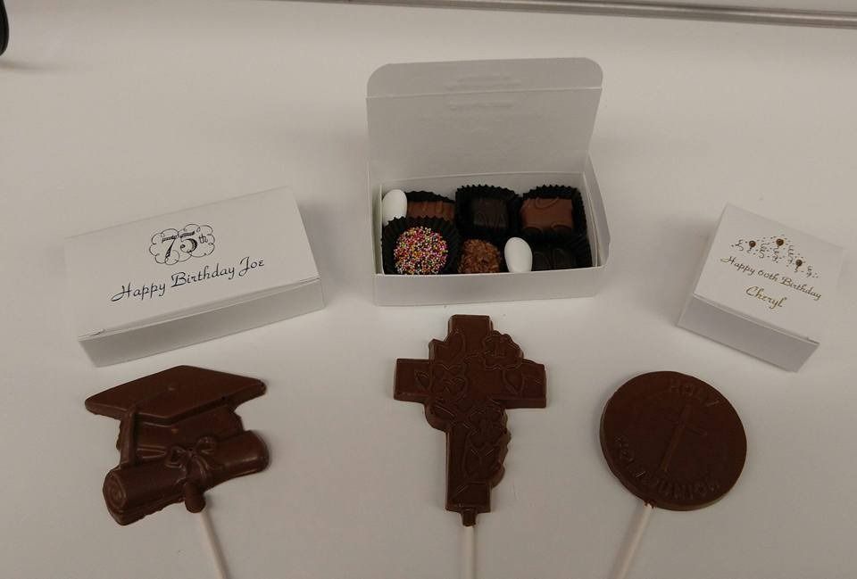 Chocolate graduation treats: box of chocolates, chocolate lollipops shaped as a cap, cross, circle; white boxes.