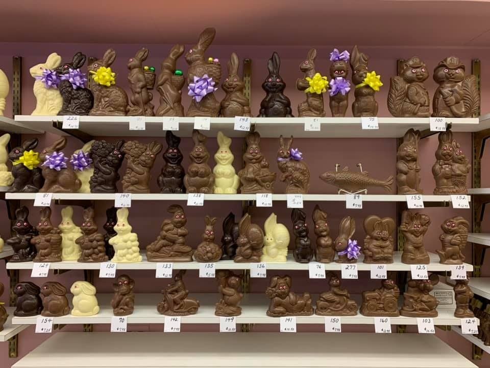 Shelves of chocolate bunnies, squirrels, and a fish displayed in a shop. Some are decorated with flowers.