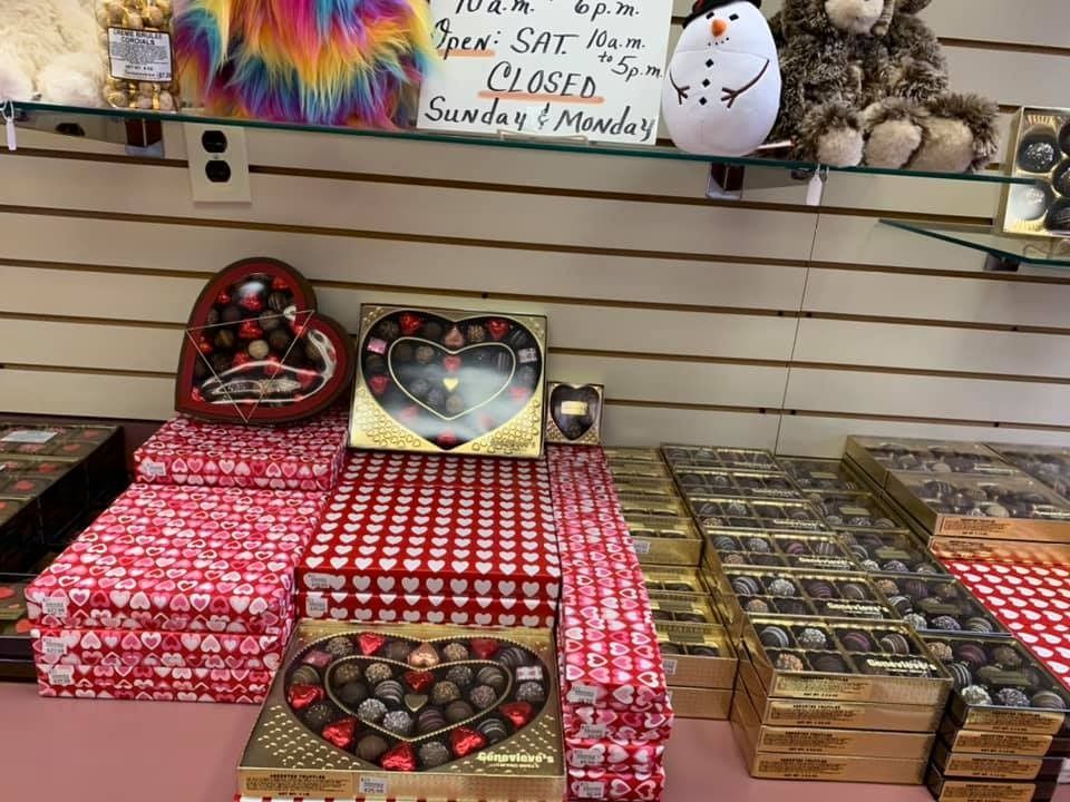Chocolate boxes, heart-shaped and rectangular, on display in a store. Red and gold packaging.