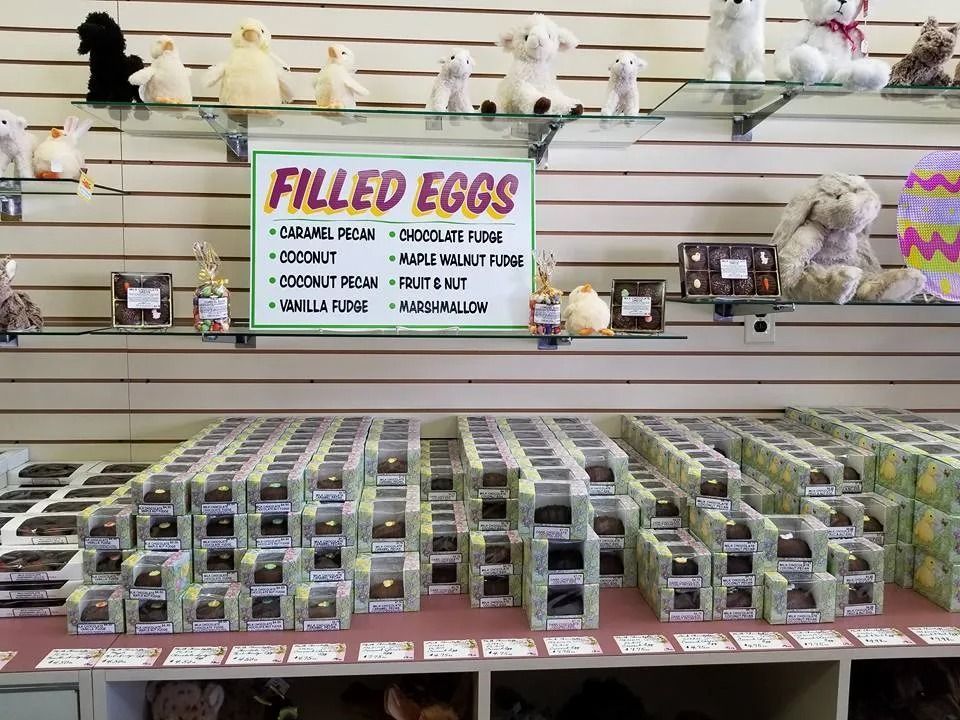 Candy store display with boxes of chocolate eggs and stuffed animals on shelves.