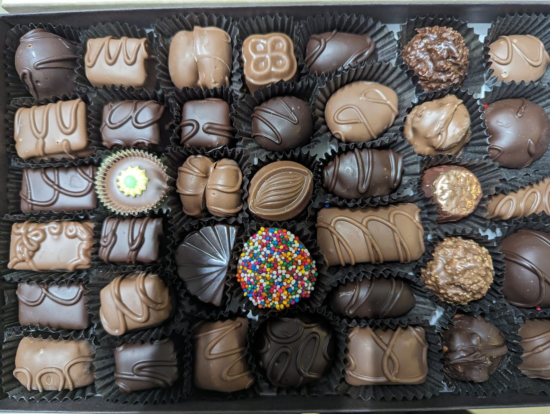 Box of assorted chocolates in various shapes and shades of brown.