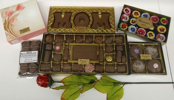 A variety of gift boxes filled with chocolates, including a MOM-shaped set, and a single red rose on a white surface.