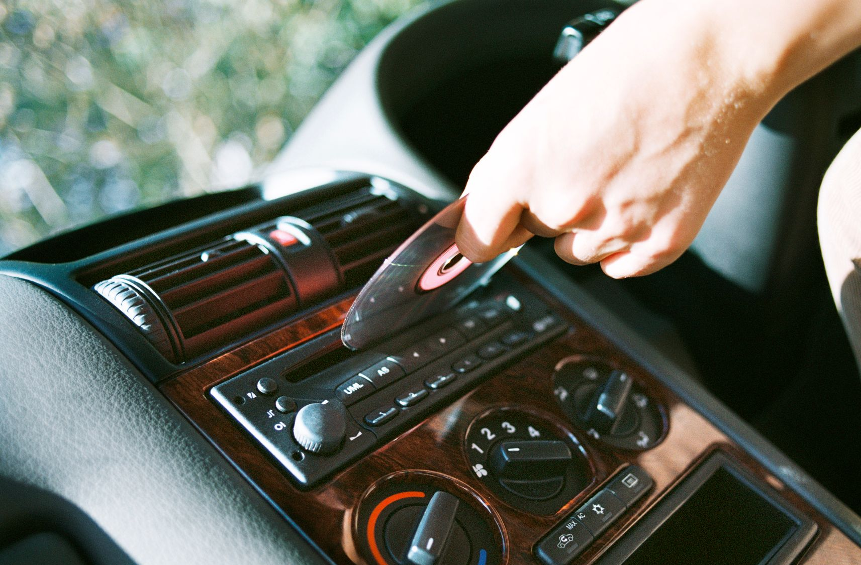 Hand inserting a CD into a car stereo. Brown wooden dashboard, vents visible.