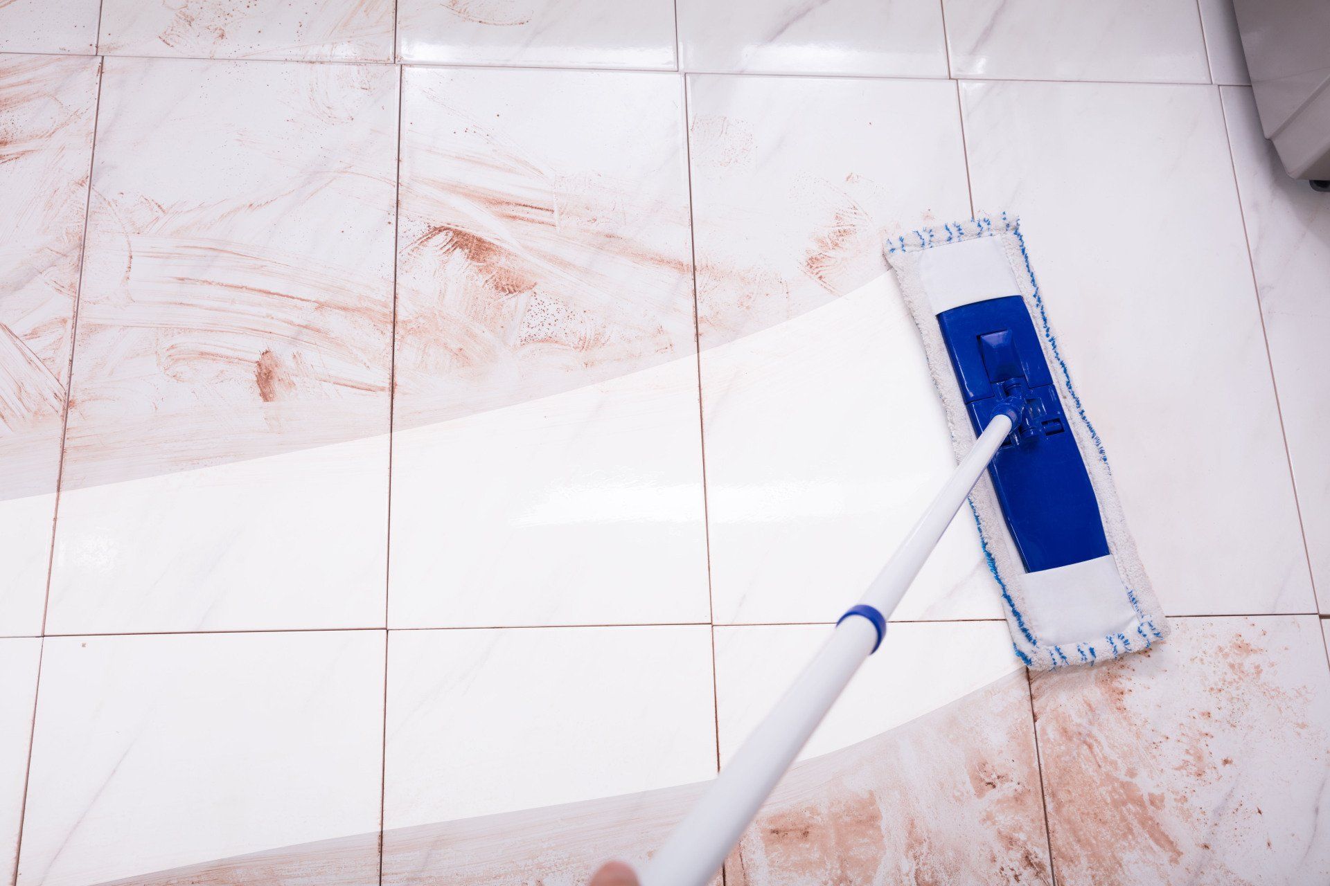 Blue mop cleaning a dirty white tiled floor with red stains
