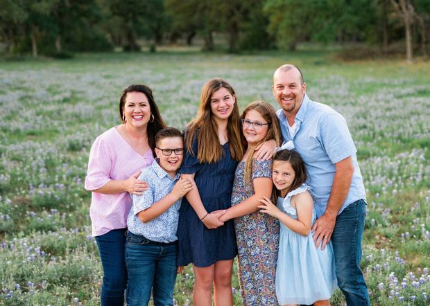 Family of six standing together in a grassy field, smiling at the camera.