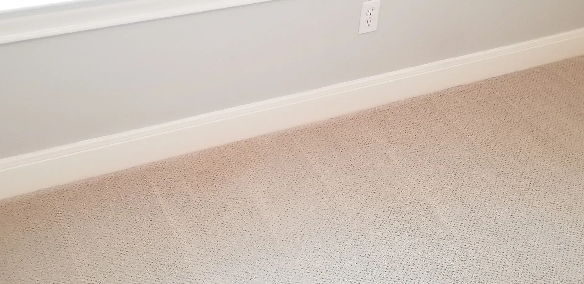 White baseboard along a light gray wall above beige carpet in a corner of a room