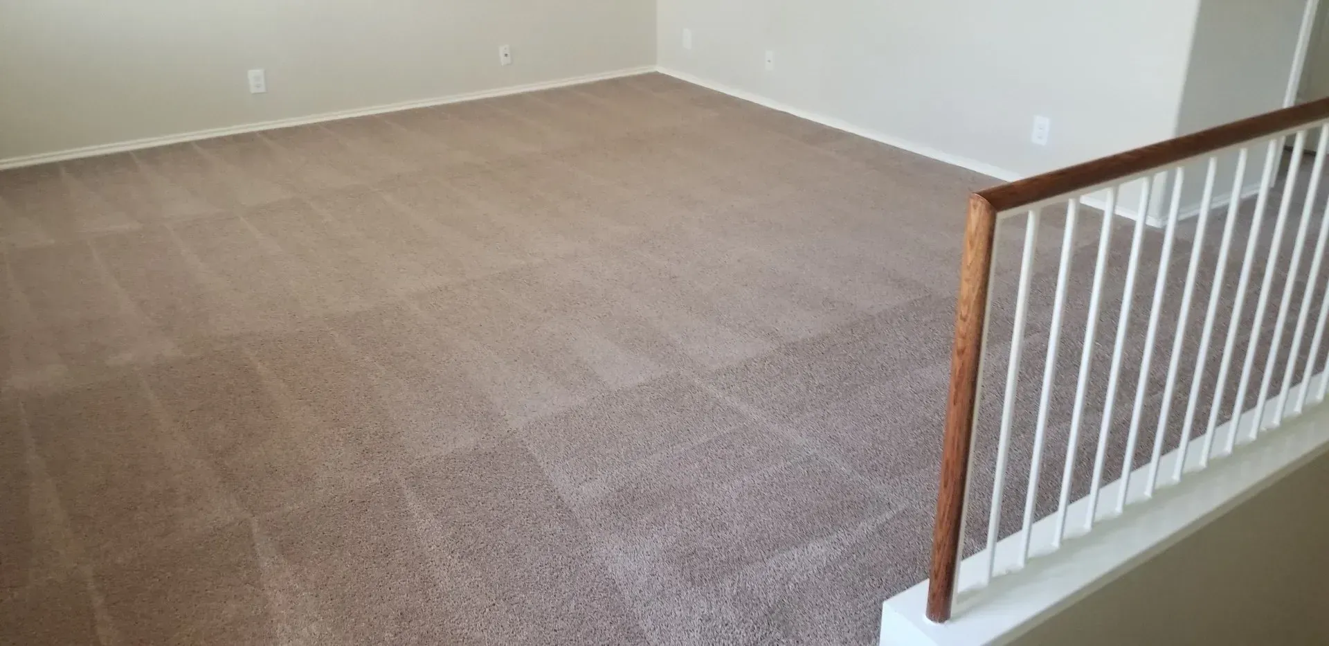 Empty carpeted room with beige walls and a white stair railing