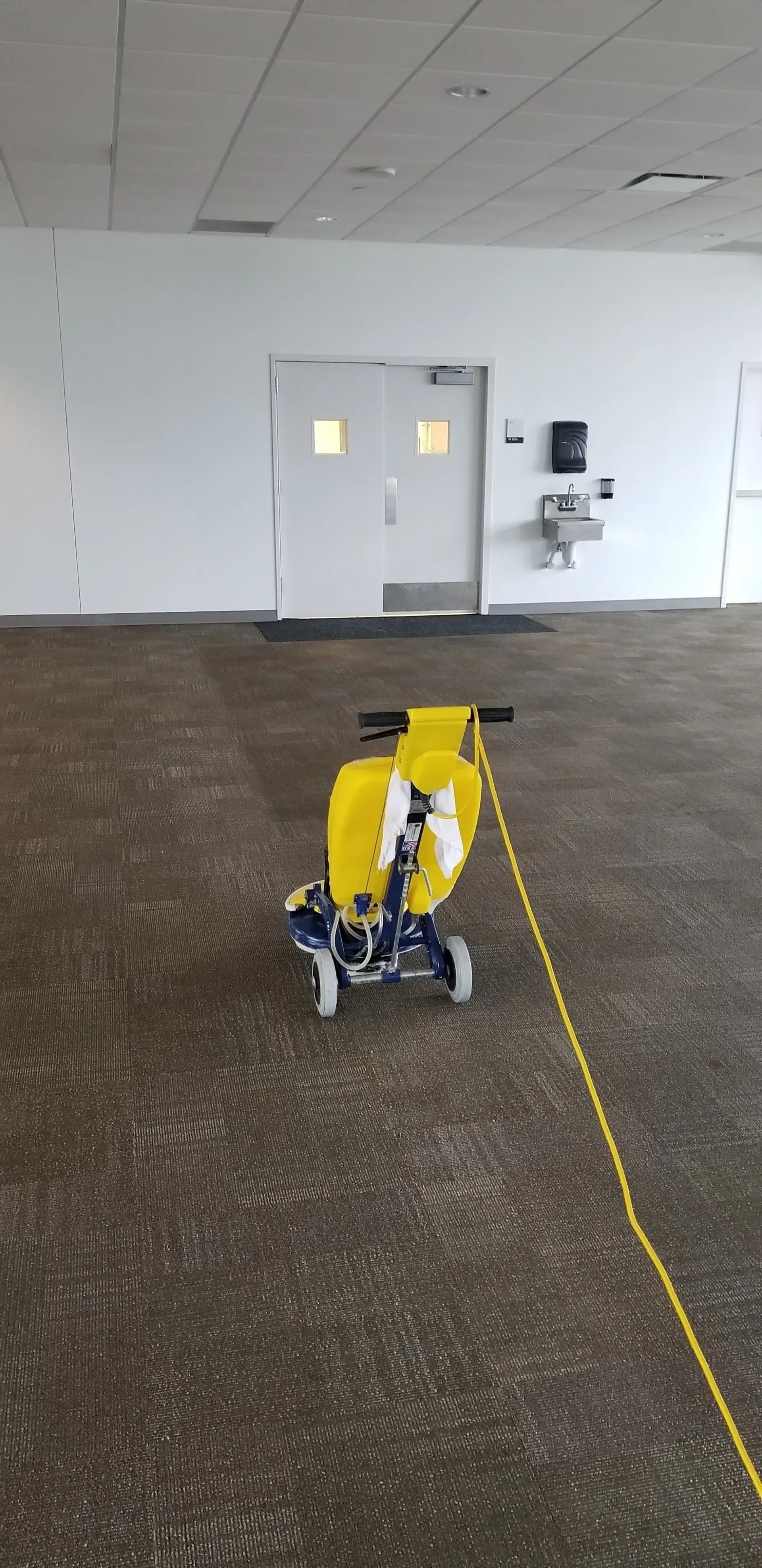 Yellow robotic rover in an empty indoor room with double doors and a tiled floor