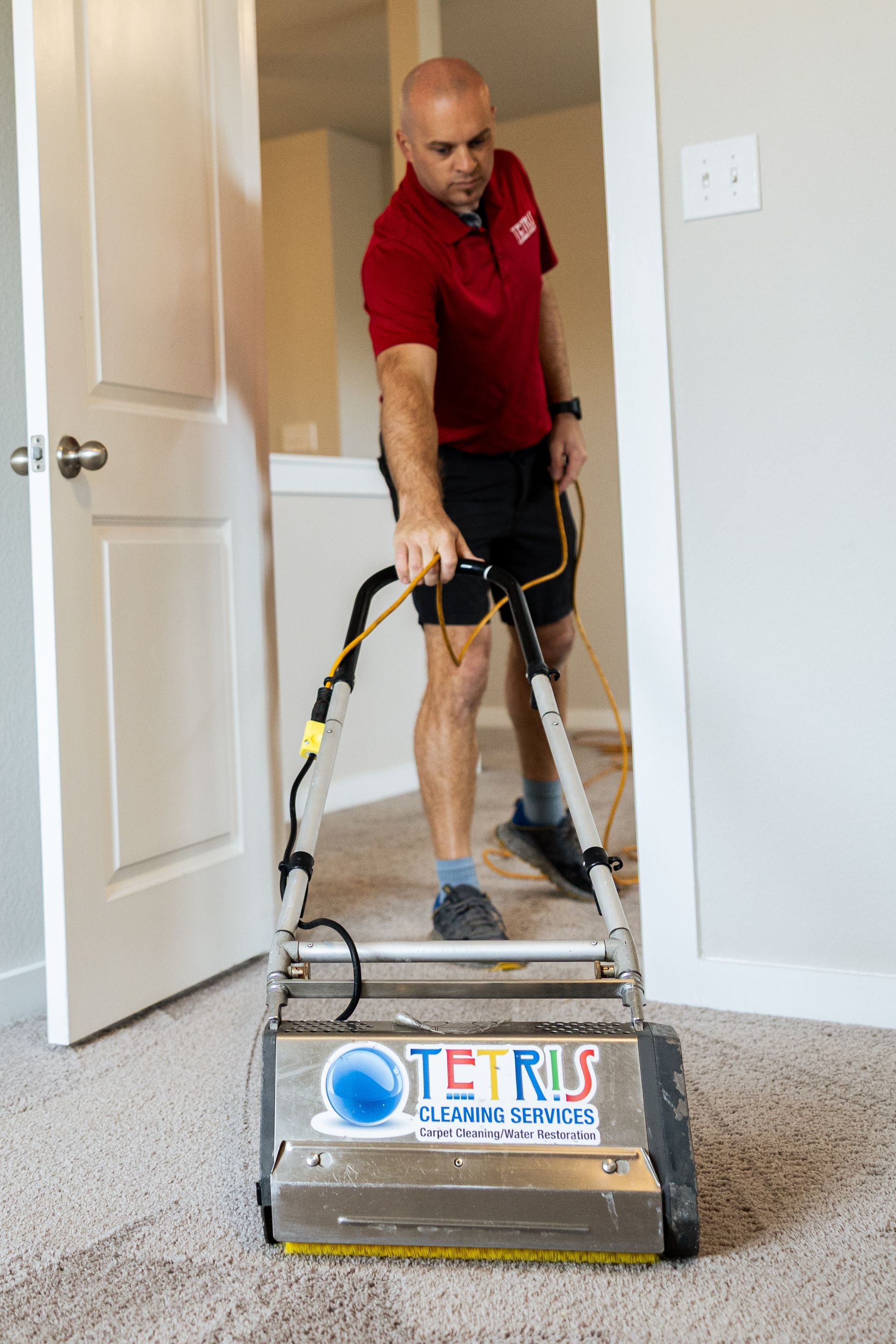 Technician using a carpet cleaner in a doorway, cleaning beige carpet with a red shirt and yellow machine.
