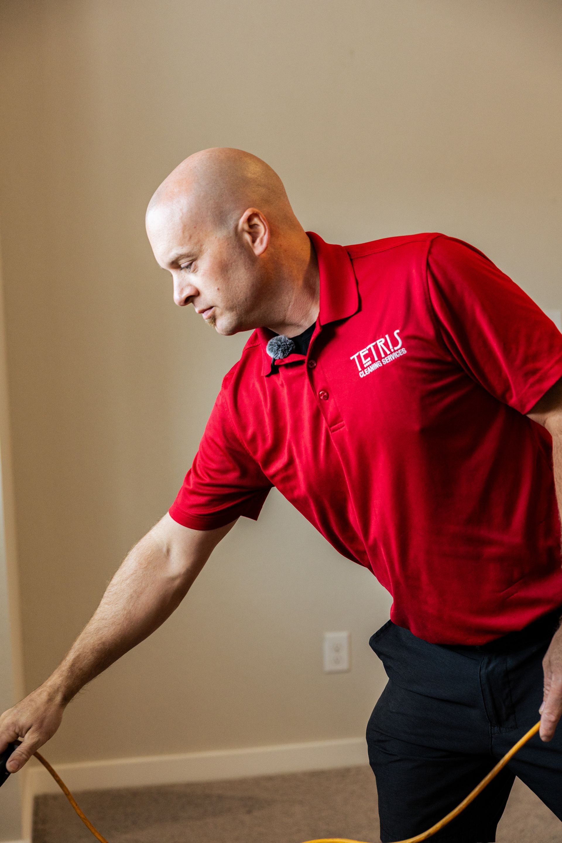 Man in red polo shirt leaning over, reaching toward something with a tool in a room with beige walls.