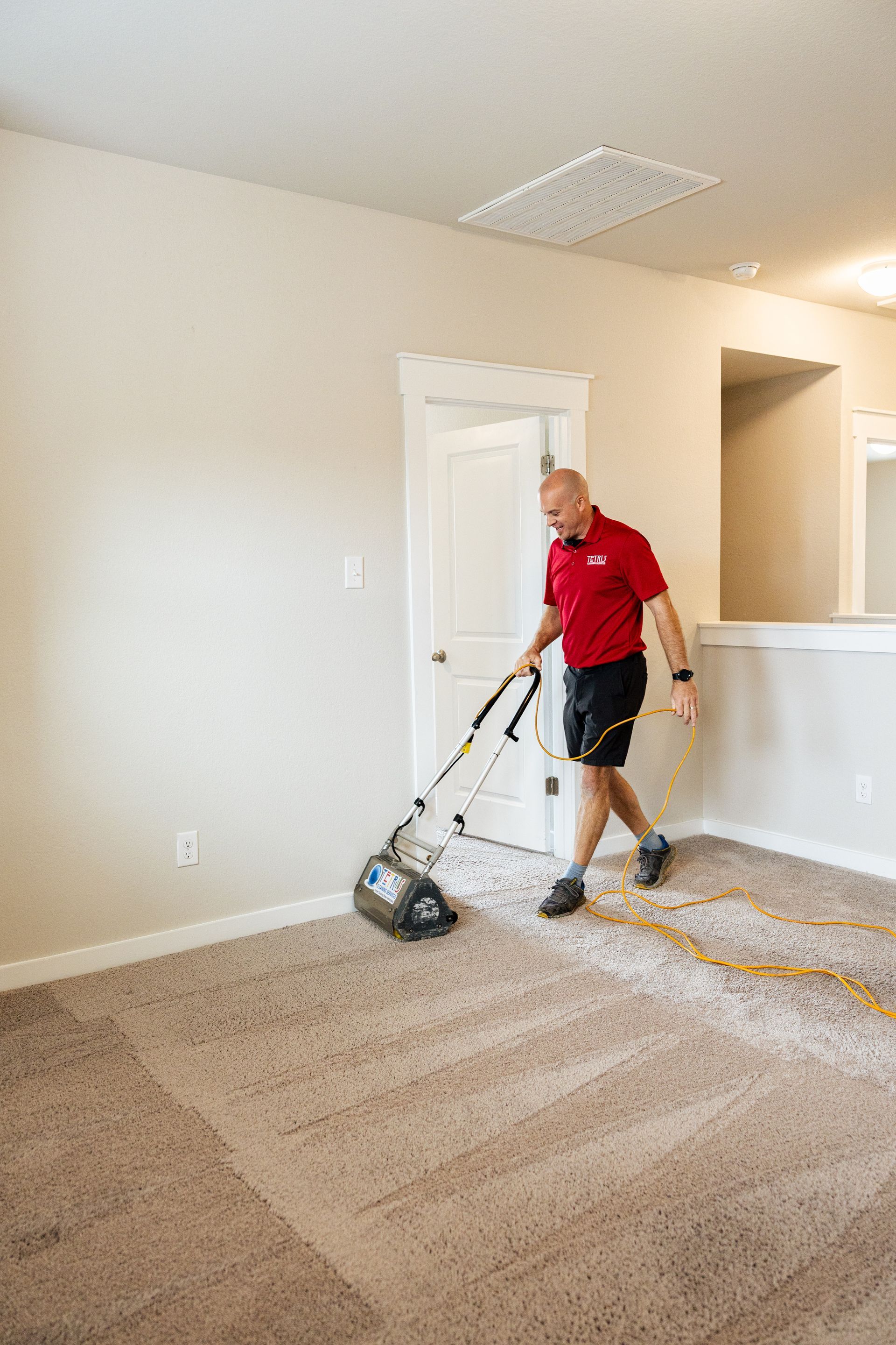 Man vacuuming carpet in a beige room with white trim and a hallway opening