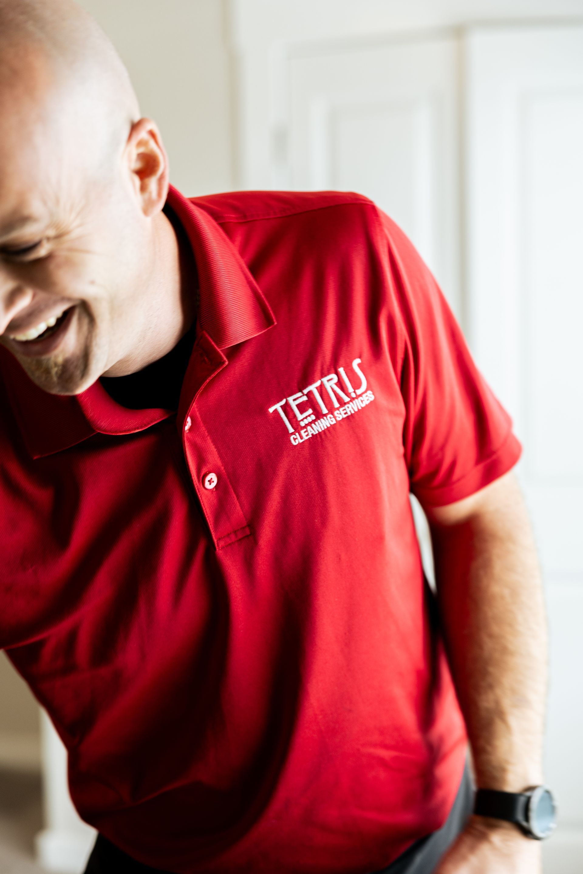 Man in a red polo shirt with a Tetris logo, leaning forward and smiling indoors.