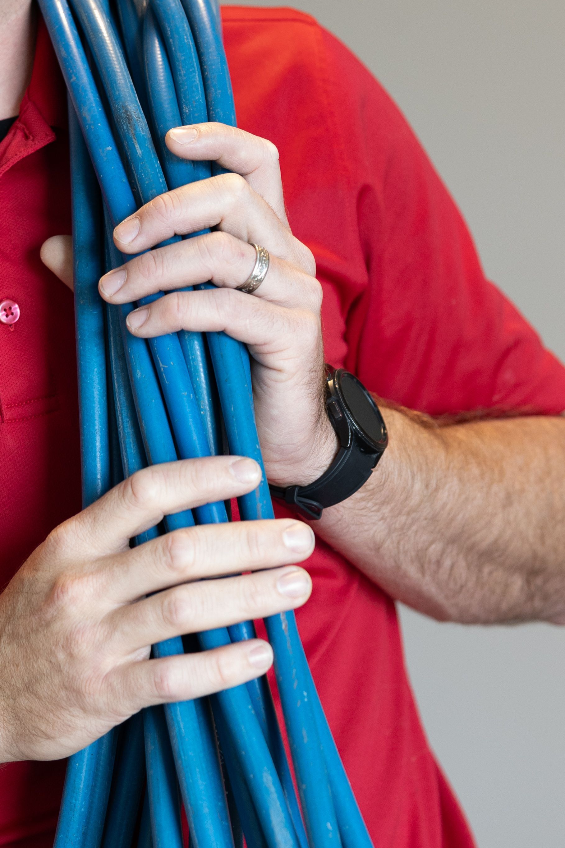 Hands holding coiled blue cables, with a person in a red shirt and black wristwatch in the background