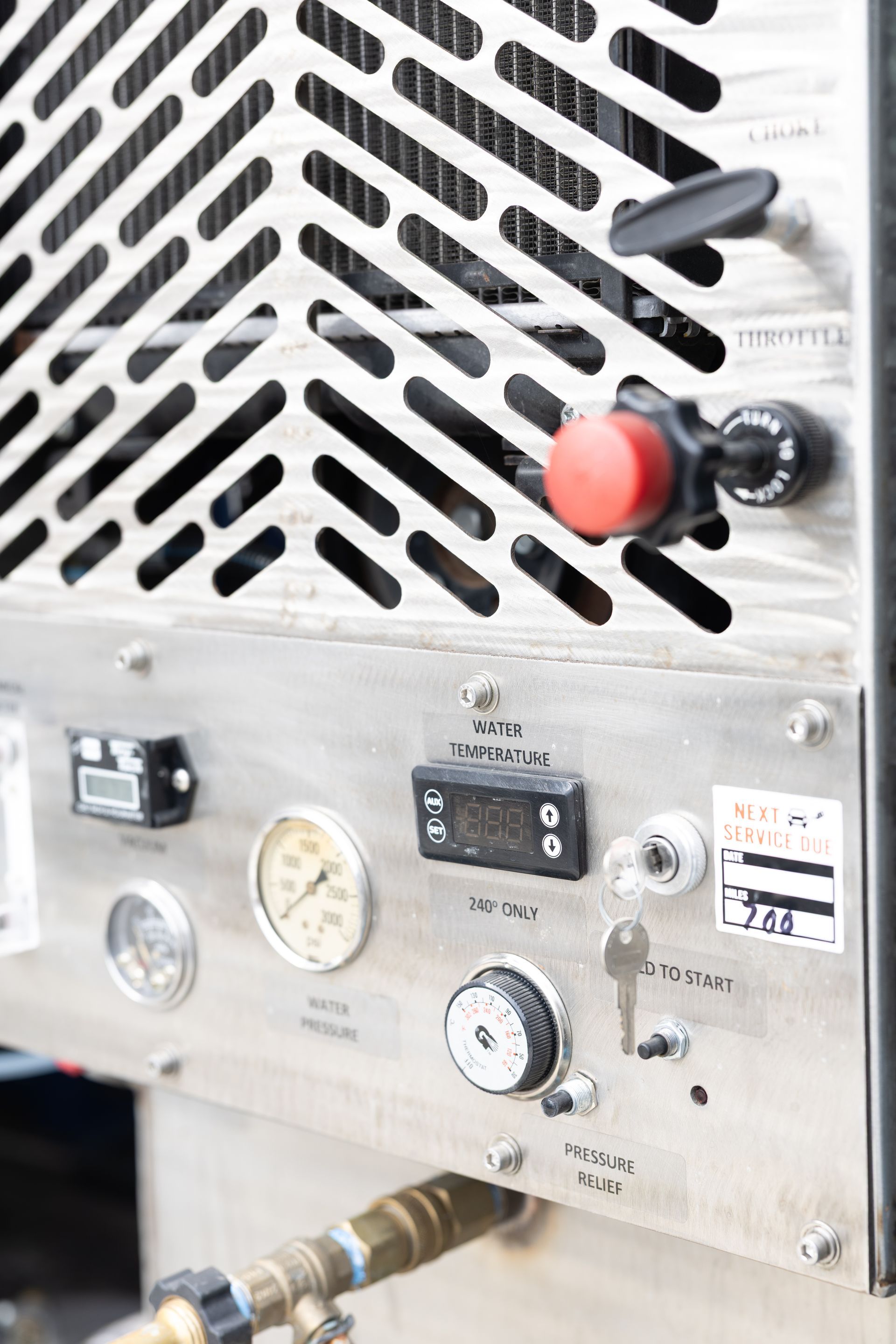 Close-up of industrial machine control panel with vents, gauges, switches, and red emergency stop button