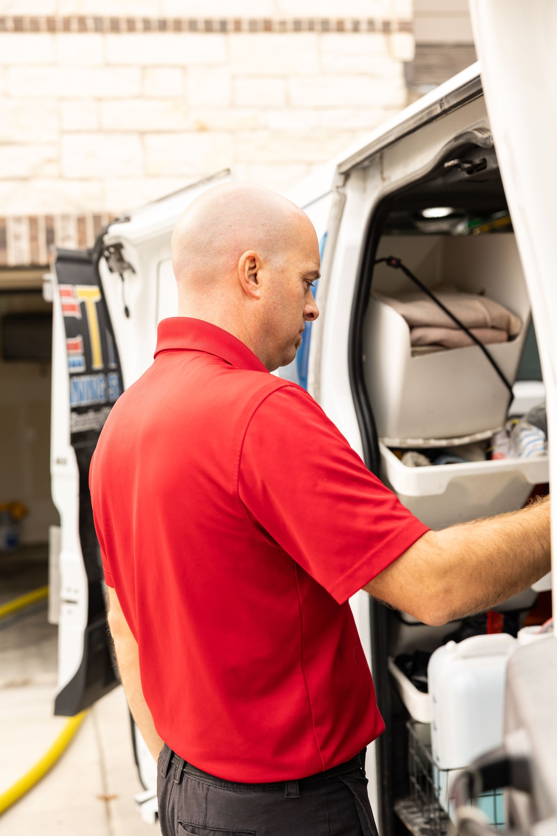 Man in red shirt working inside a white service van in a garage