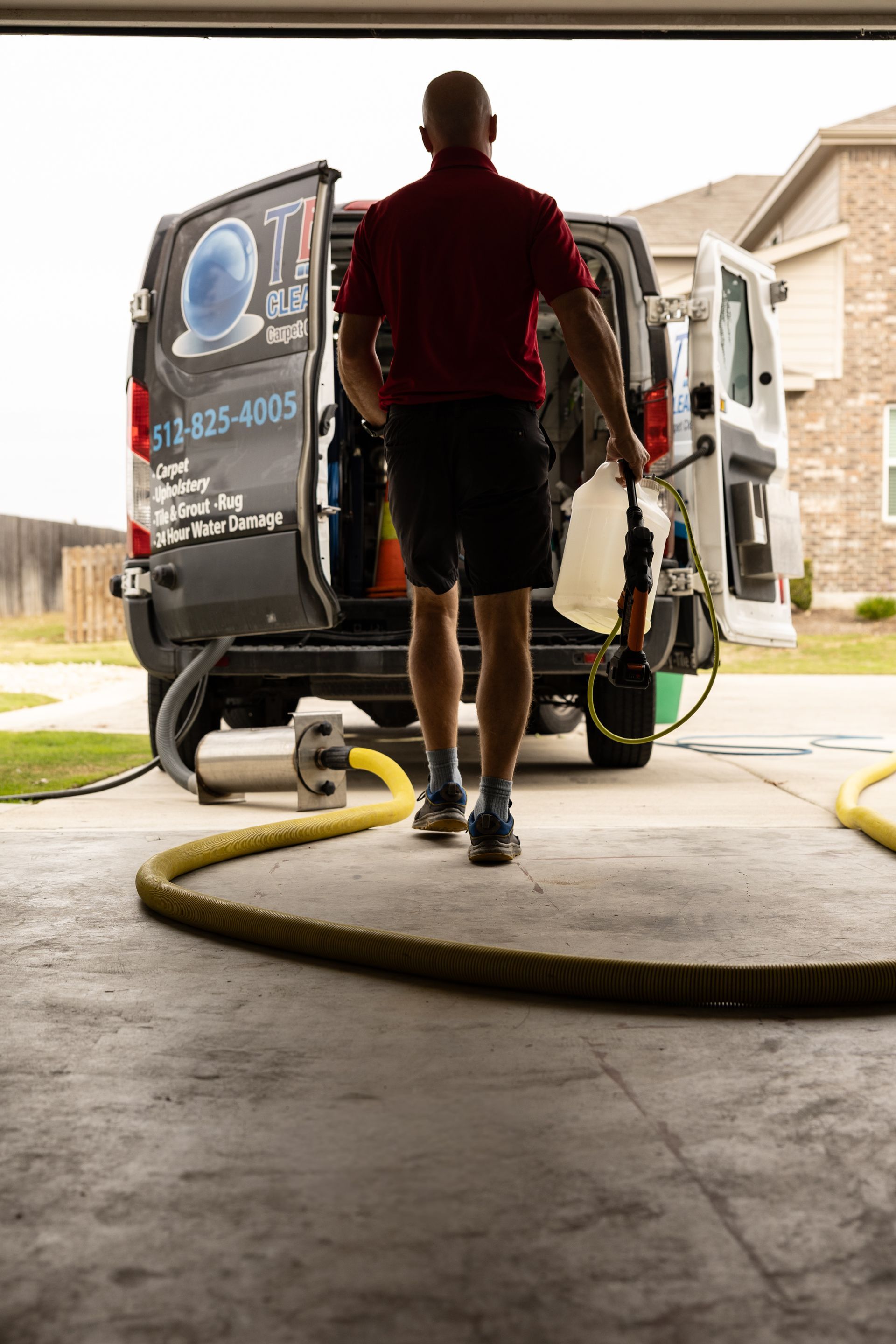 Person walking into a garage with a carpet-cleaning van and hose equipment.