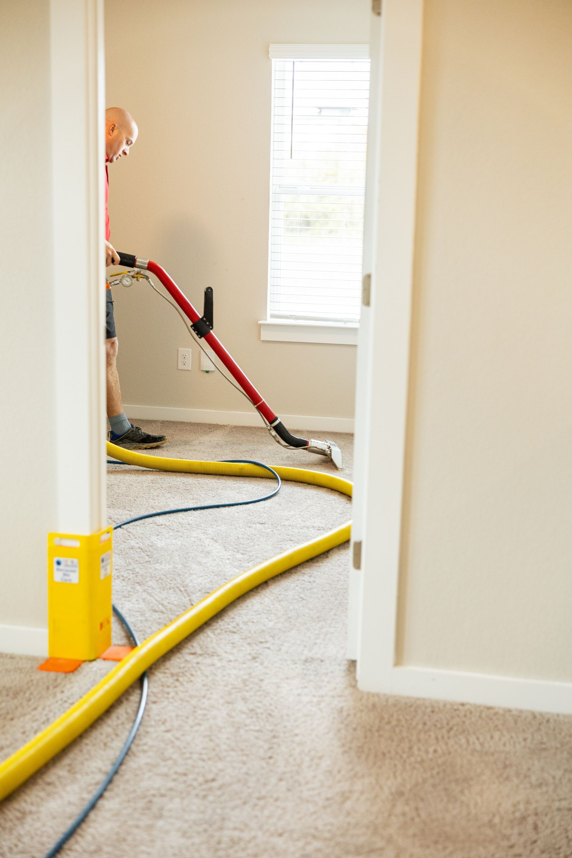 Worker using a red vacuum hose in a carpeted hallway during cleaning or restoration work