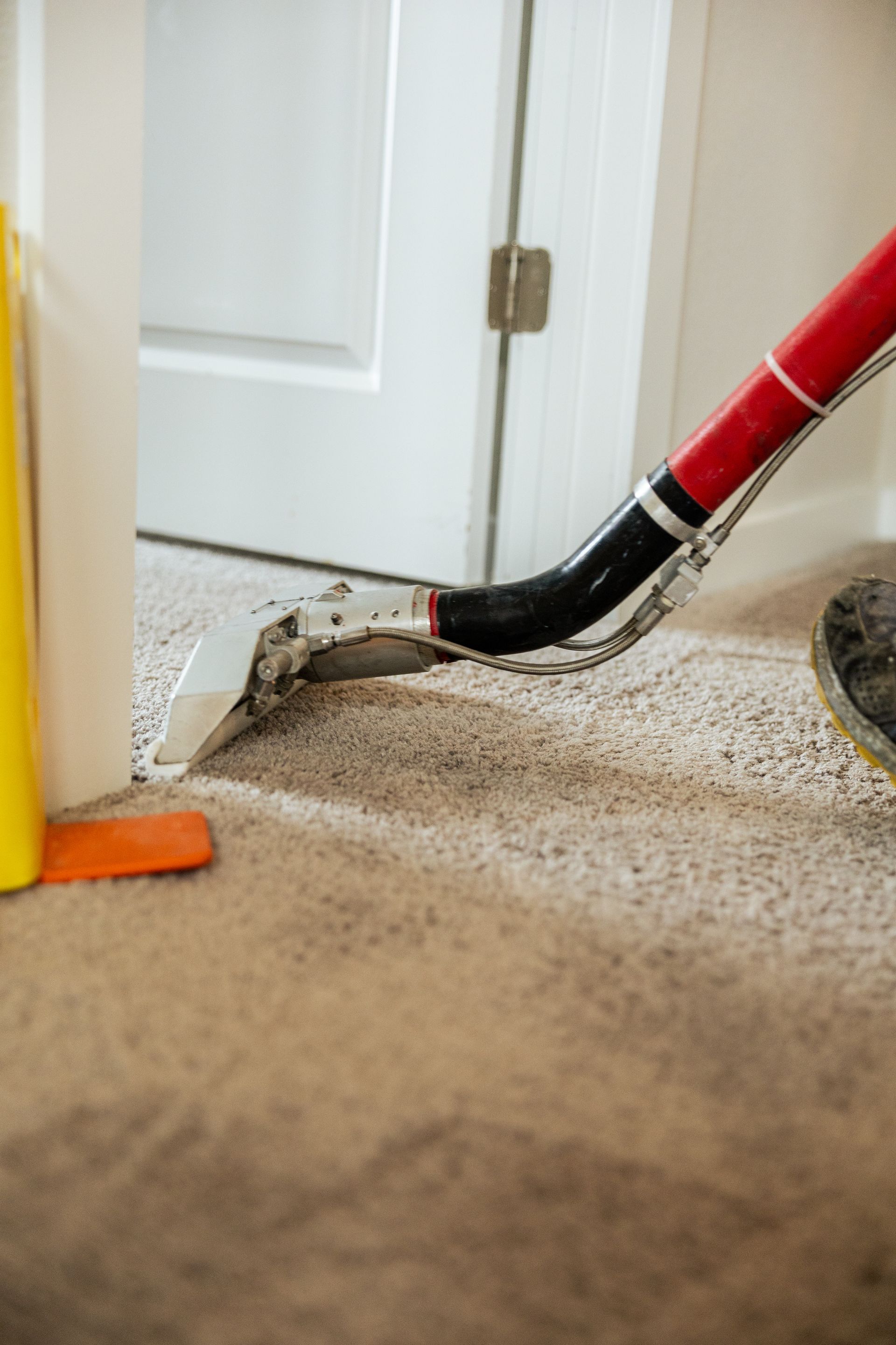 Vacuum hose cleaning debris along a baseboard near a white door and carpet edge
