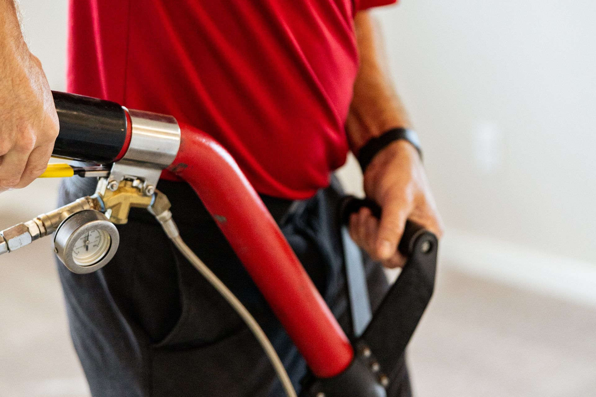 Close-up of a cyclist holding handlebars and a red bike frame, with a pressure gauge attached to the tire valve.
