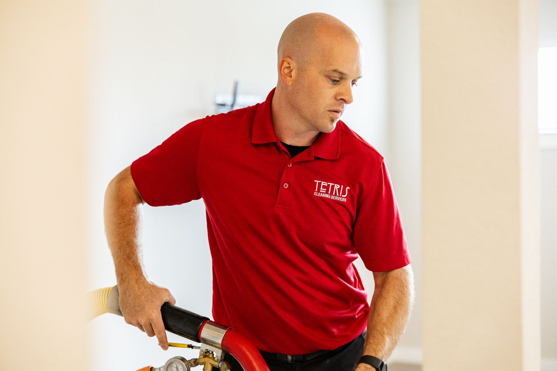 Man in a red polo shirt using a tool in a bright indoor hallway