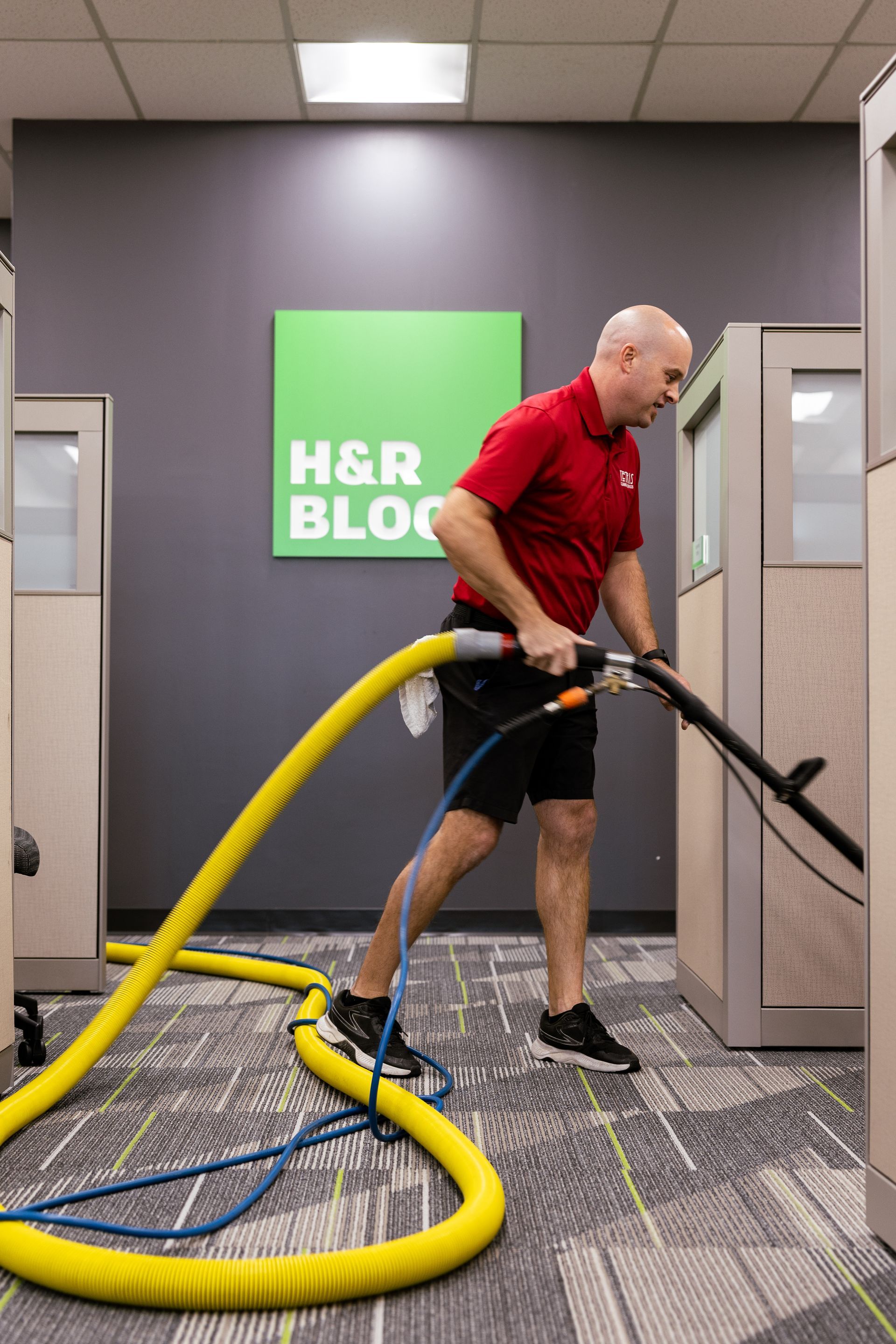 Worker vacuuming a carpeted office hall with a yellow hose near H&R Block offices