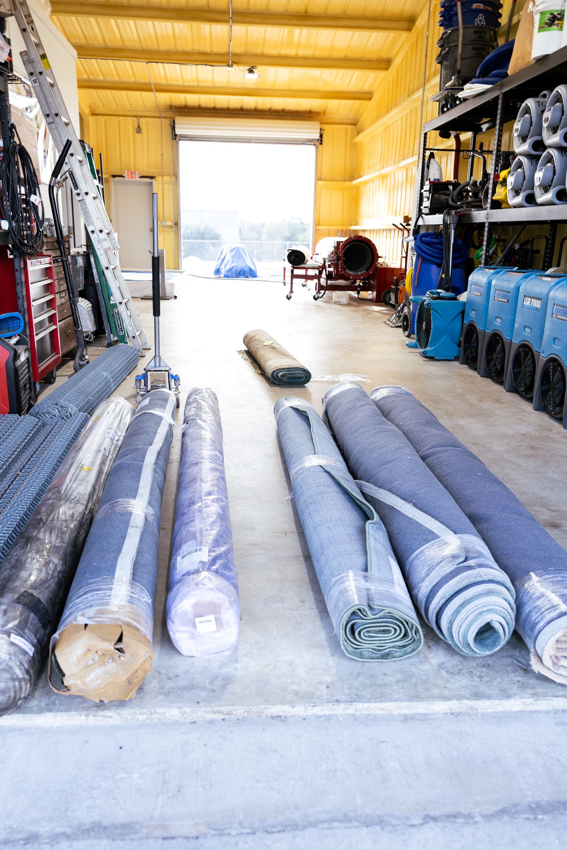 Warehouse aisle with rolled-up carpet or flooring rolls stacked on both sides and laid on the floor.