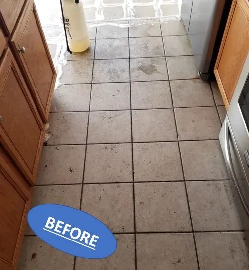 Before photo of a narrow tiled kitchen floor with a few stains and cabinets along both sides