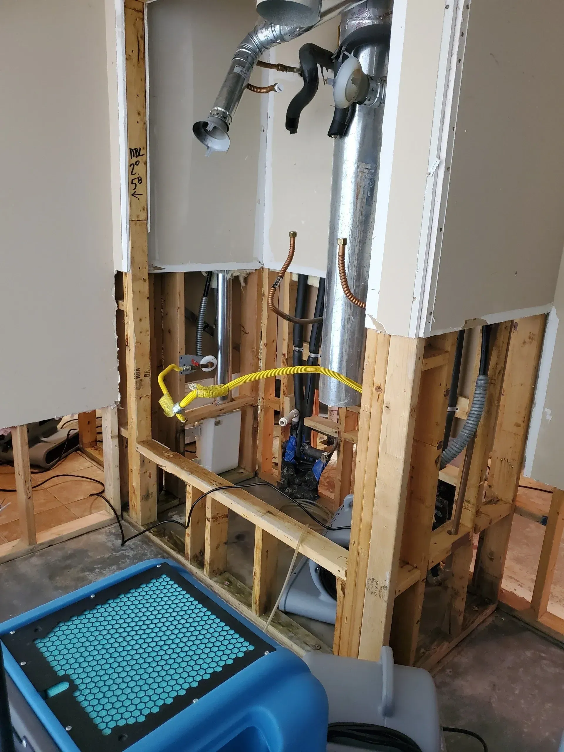 Exposed bathroom plumbing and studs with drywall removed, showing pipes and a blue tool box on the floor.