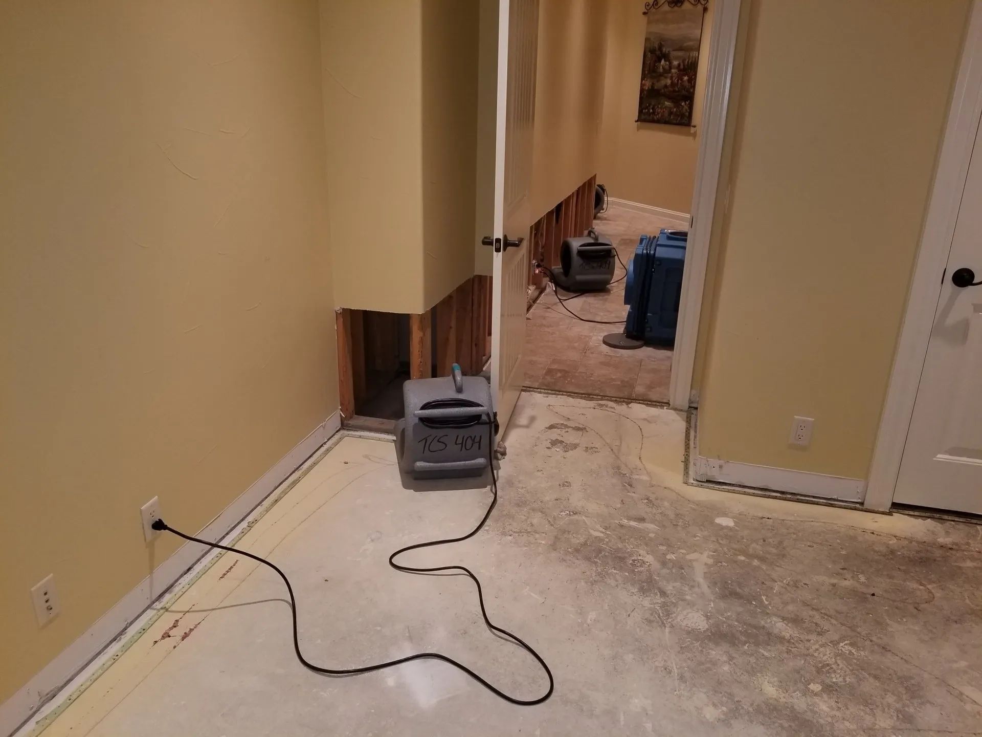 Partially carpeted hallway with a power tool and cord on the floor, next to exposed subflooring and a doorway