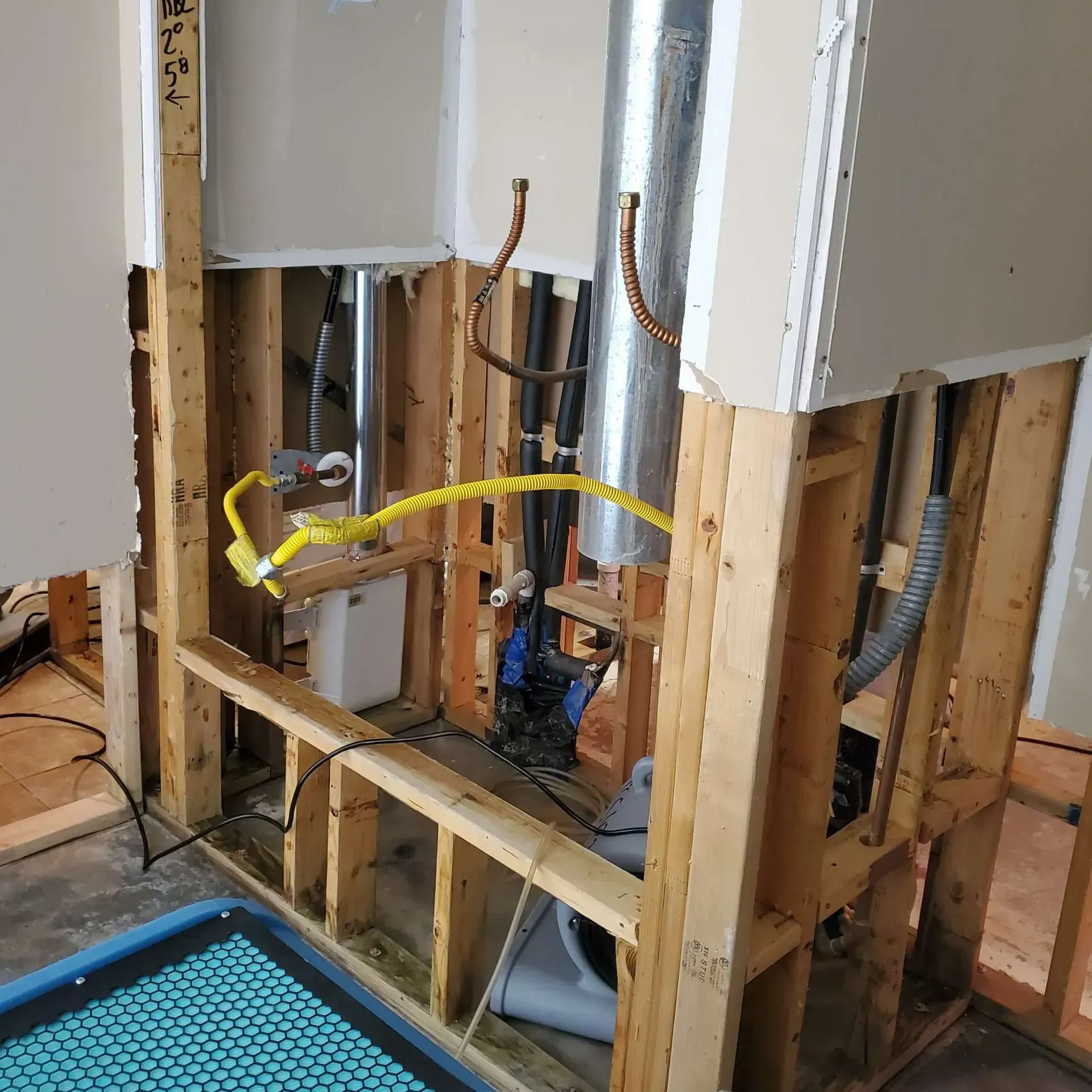 Exposed bathroom wall framing with plumbing and electrical work underway, yellow hose across studs.