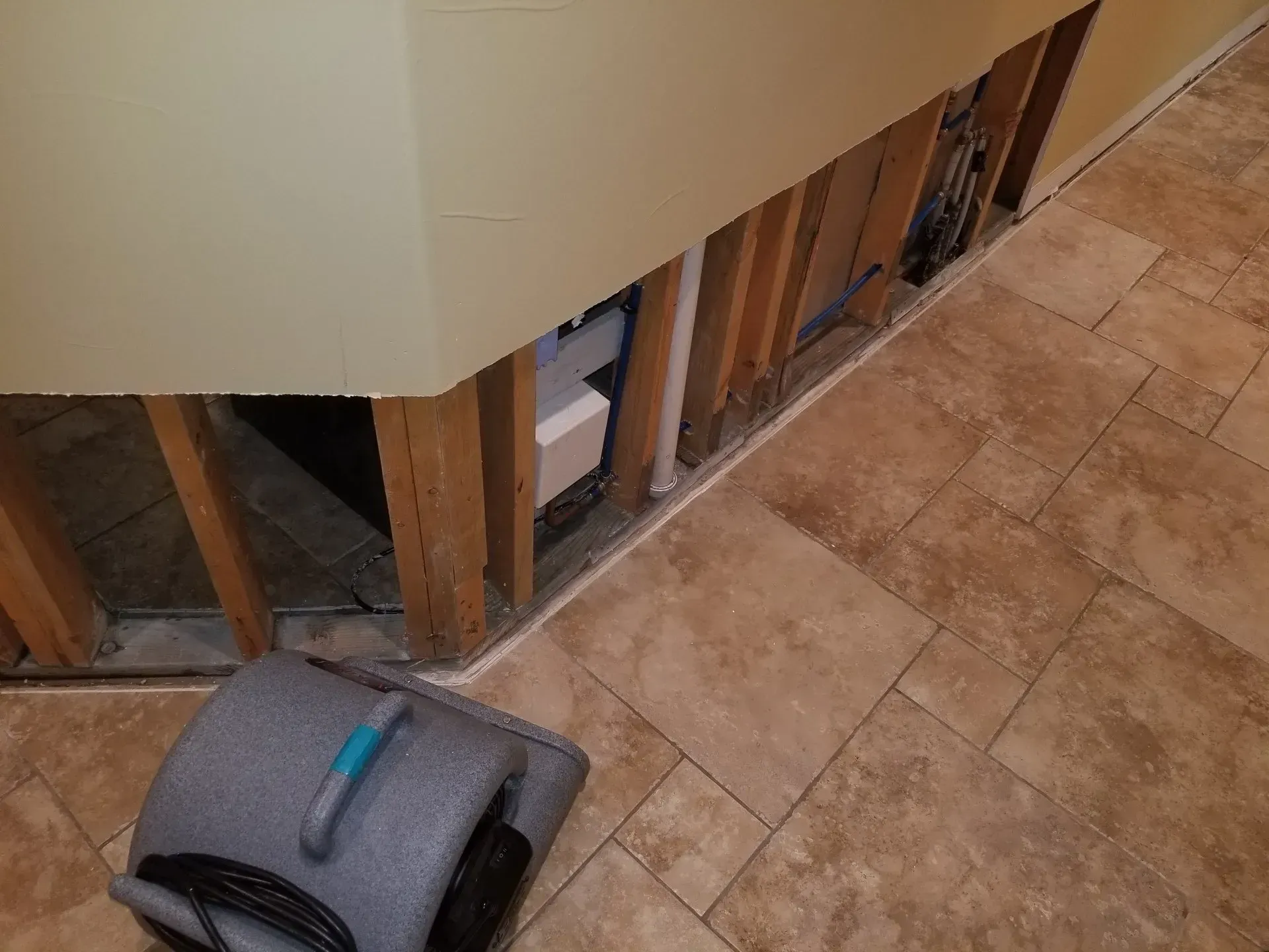 Gray suitcase on tiled floor beside a damaged wall with exposed studs and wiring.