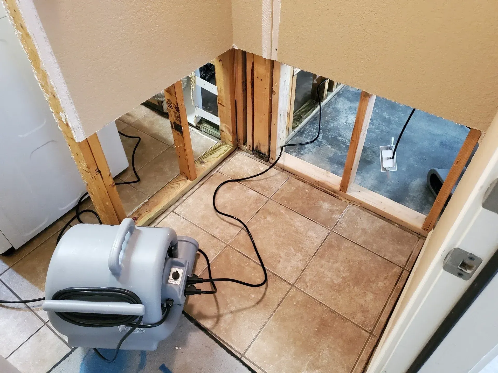 Small floor-drying fan in a partially stripped room with exposed wall framing and tile floor.