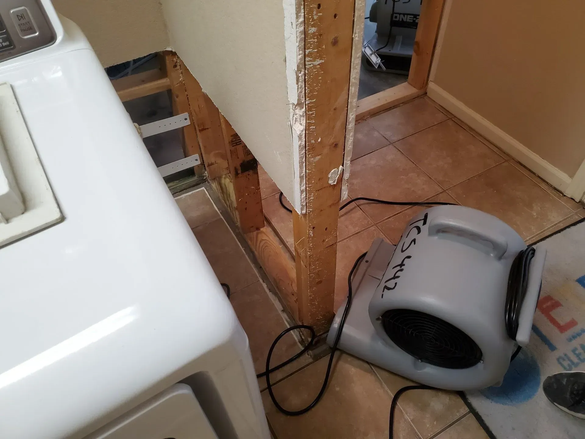Laundry room with a tipped space heater on the floor beside a white washer and exposed wall framing.