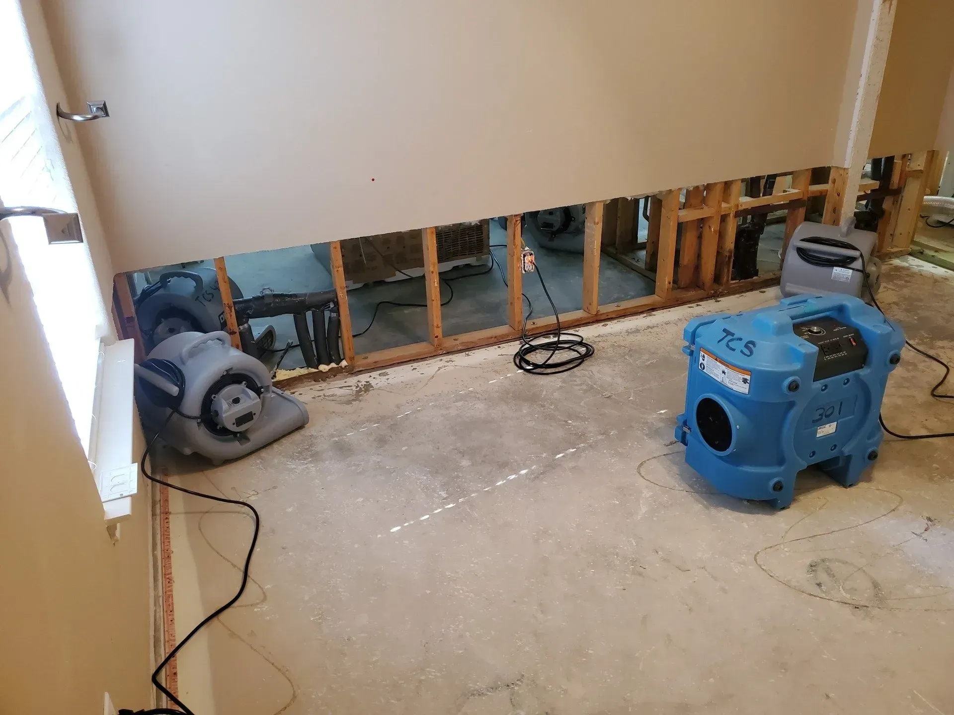 Water-damaged room under repair, with exposed wall studs and two fans on the floor