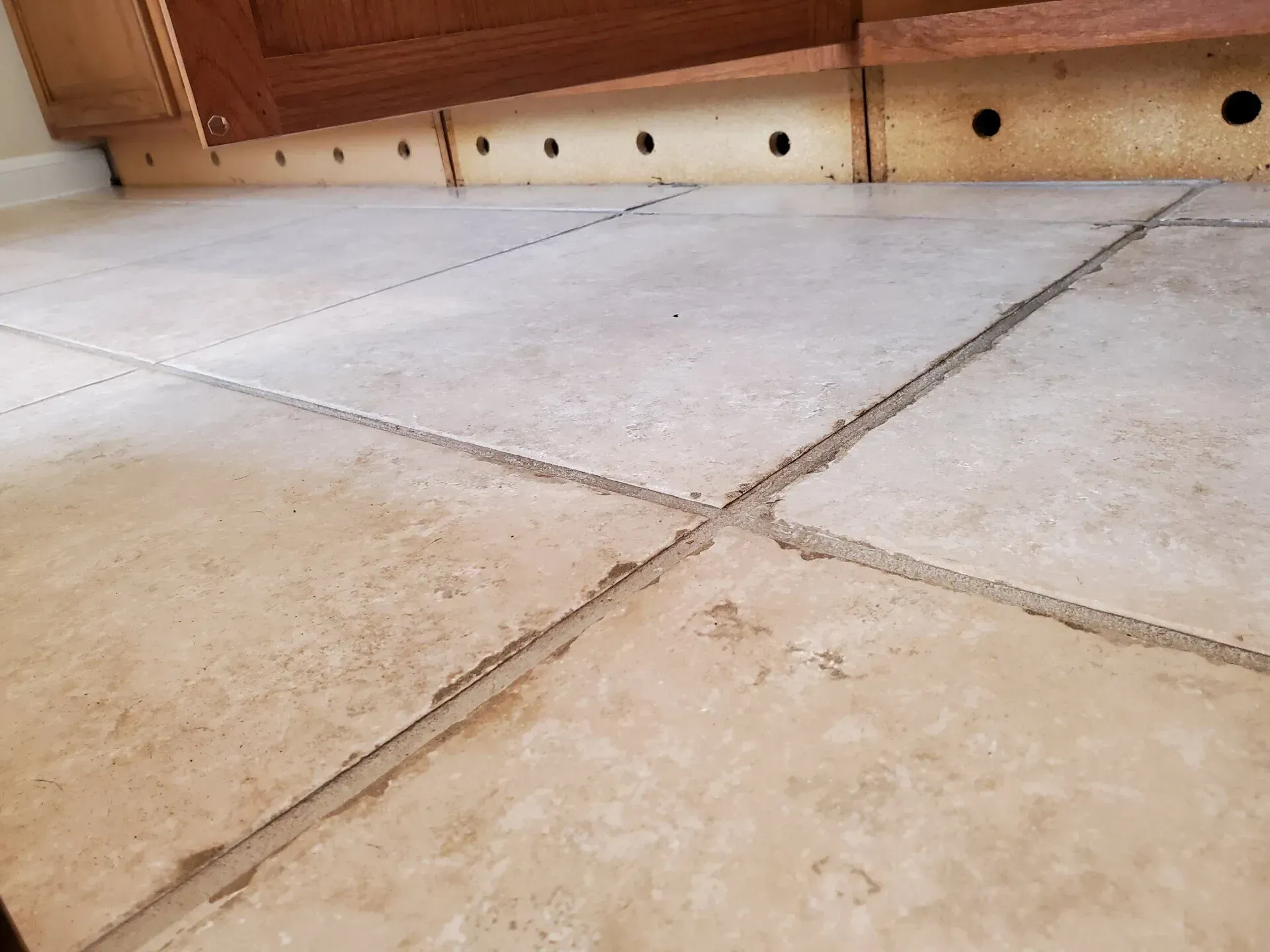 Close-up of light stone floor tiles with grout lines and a wooden wall in the background