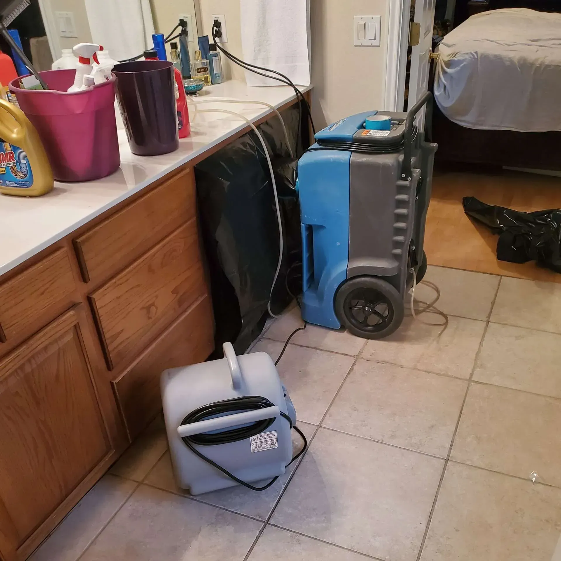 Vacuum cleaners on a tiled floor beside a wooden dresser in a bedroom