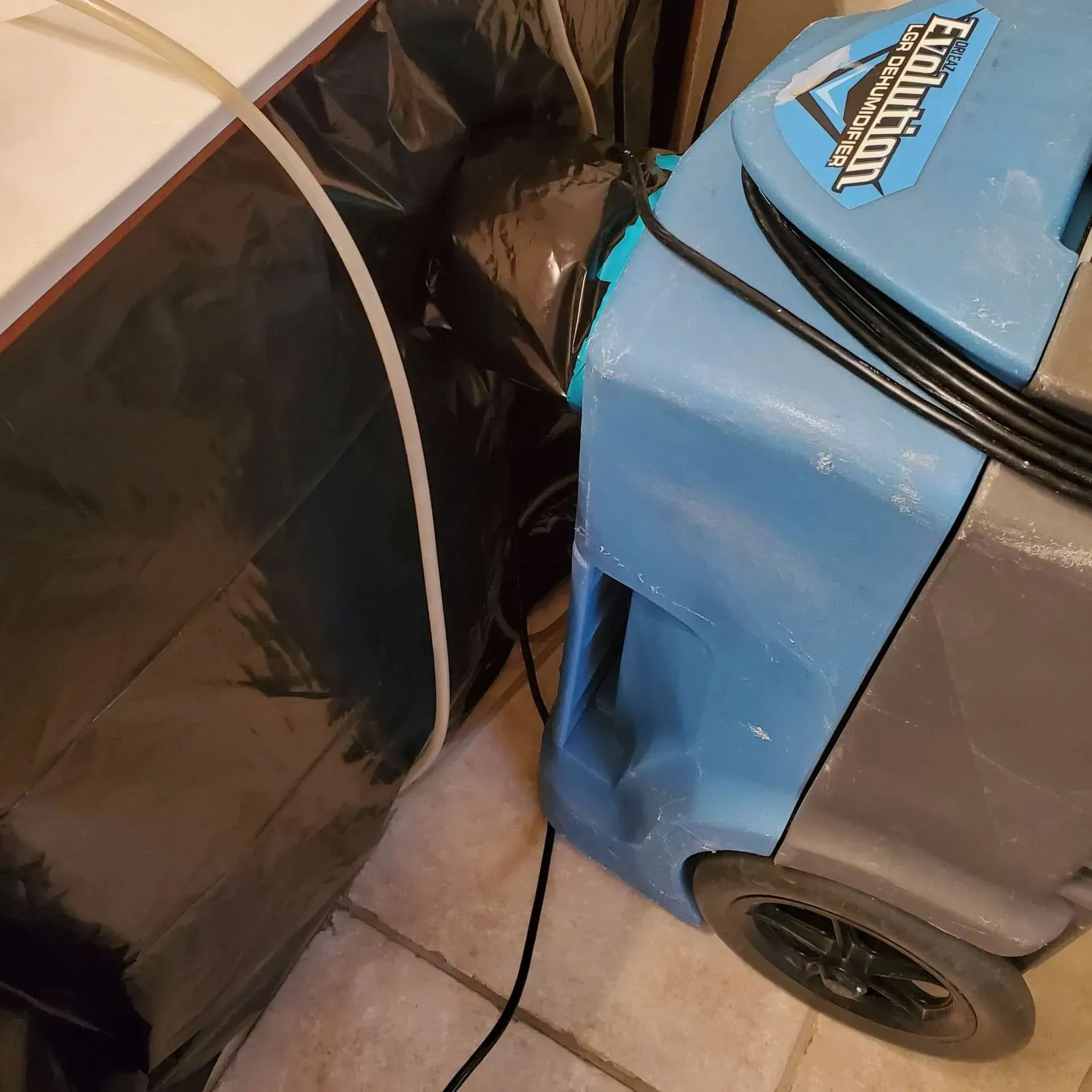 Blue and gray floor-cleaning machine beside a black padded bag on a tiled floor