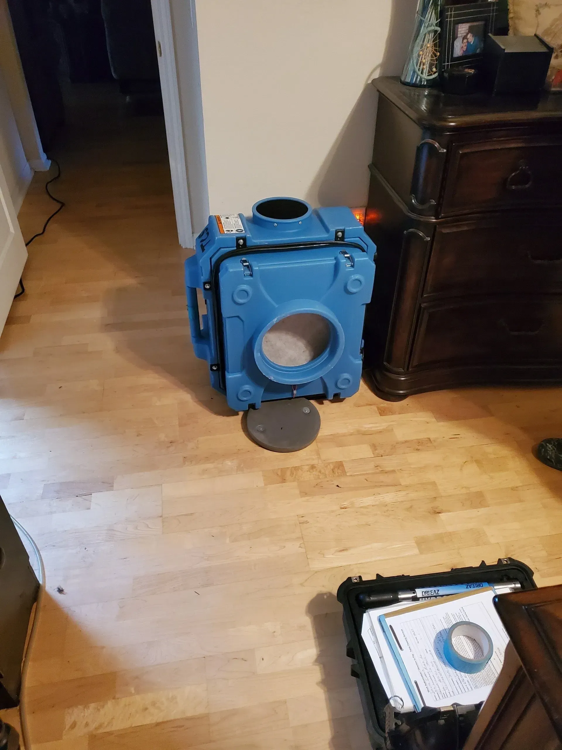 Blue portable air mover on a hardwood floor beside a dresser, with tools nearby.