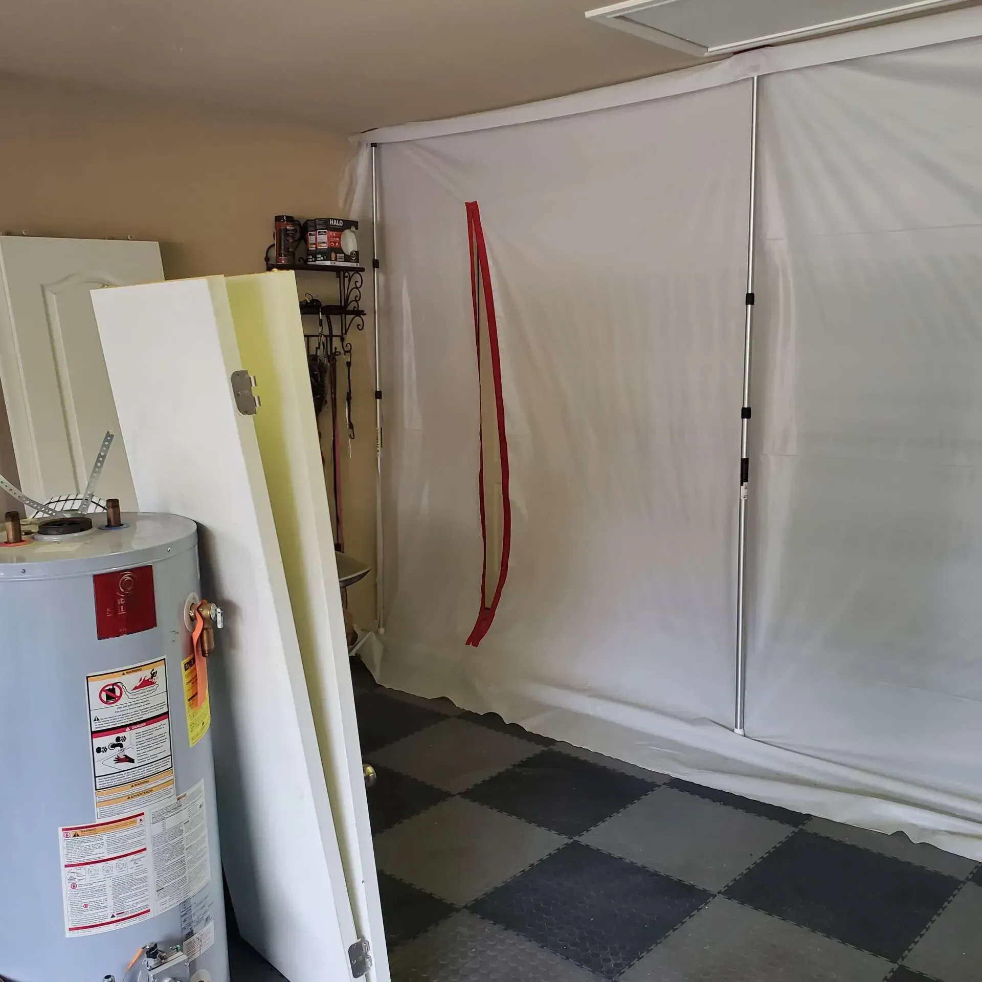 Small room with a water heater, white cabinet, and covered windows over black-and-gray checkered flooring.