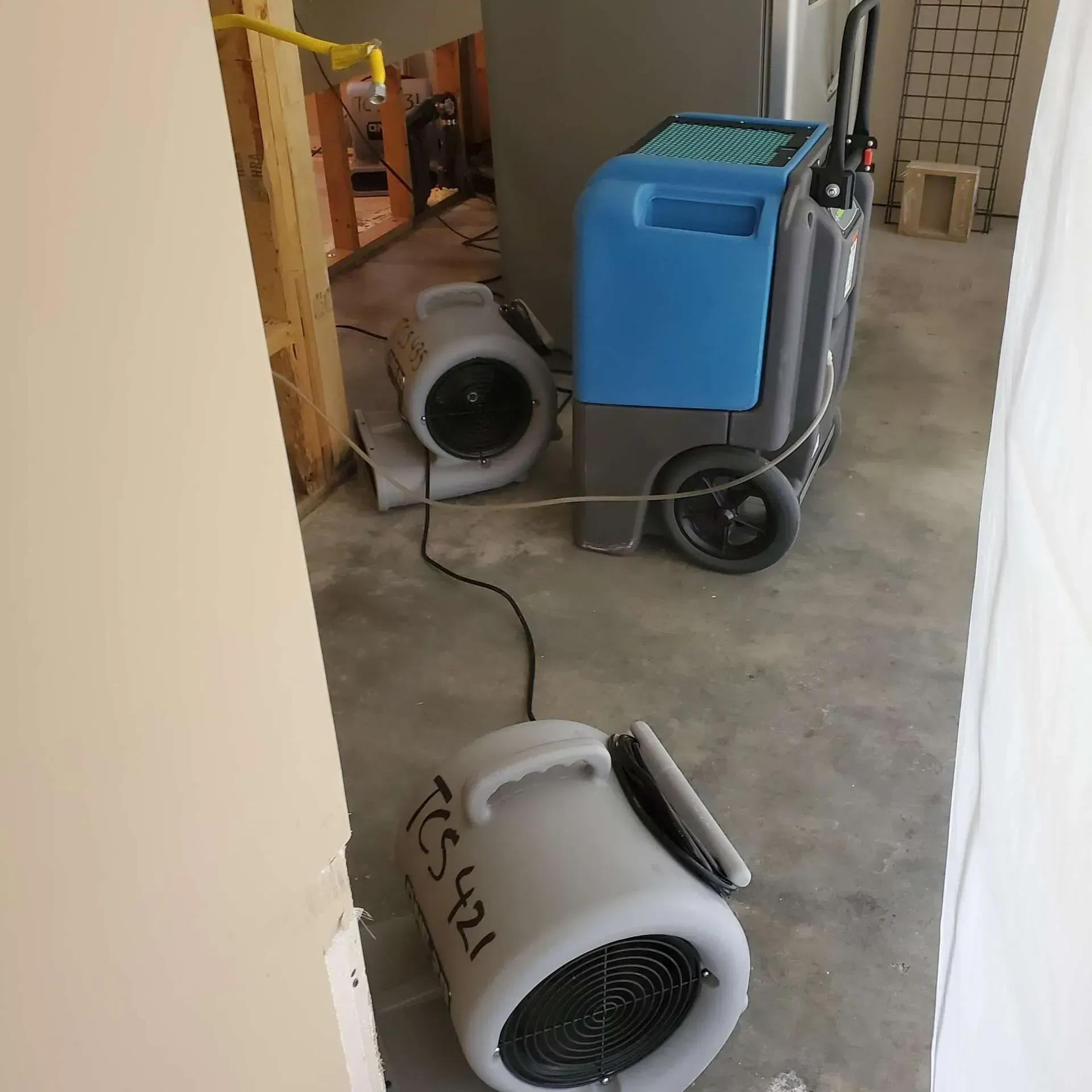 Two dehumidifiers and a blue floor-cleaning machine in a hallway with a cord across the floor