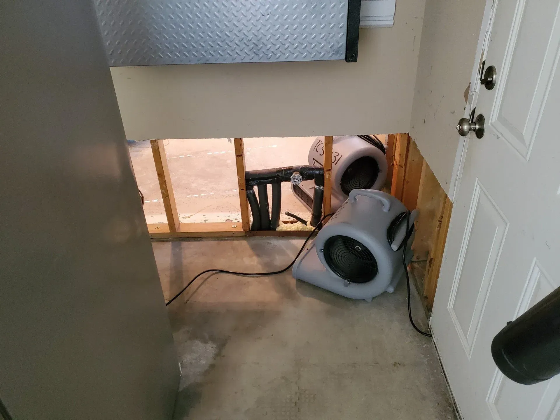 Basement hallway with a tipped gray dryer on the floor and a black cord running across the carpet.
