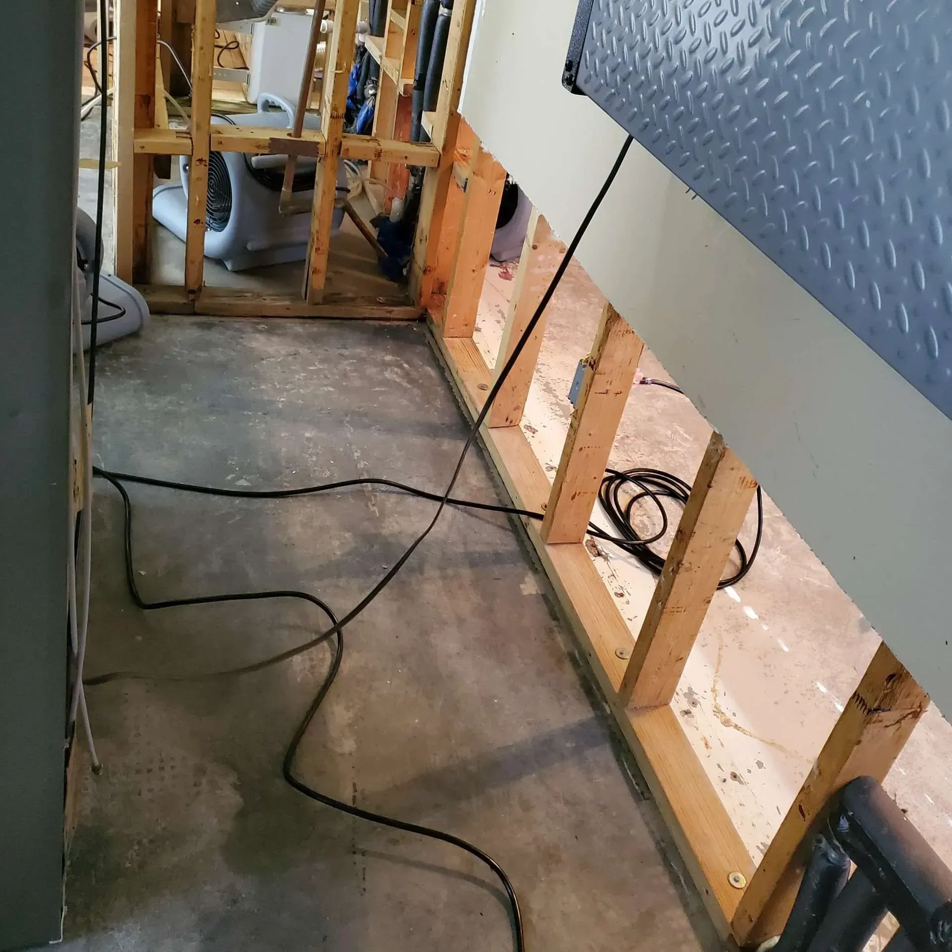 Unfinished hallway with exposed wall studs, concrete floor, and loose black cables along the wall.