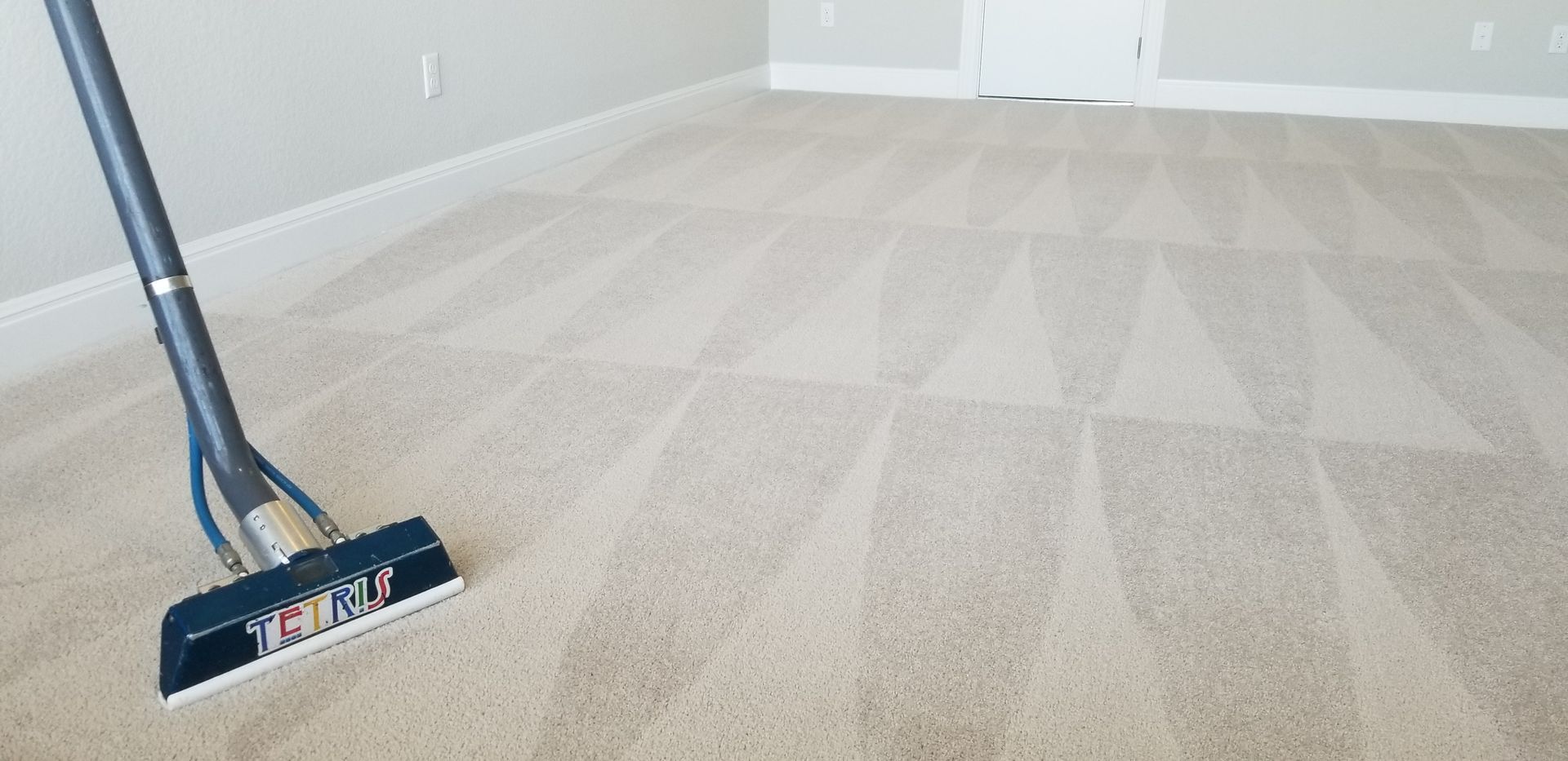 Vacuum cleaning a light beige carpet in a bright empty room
