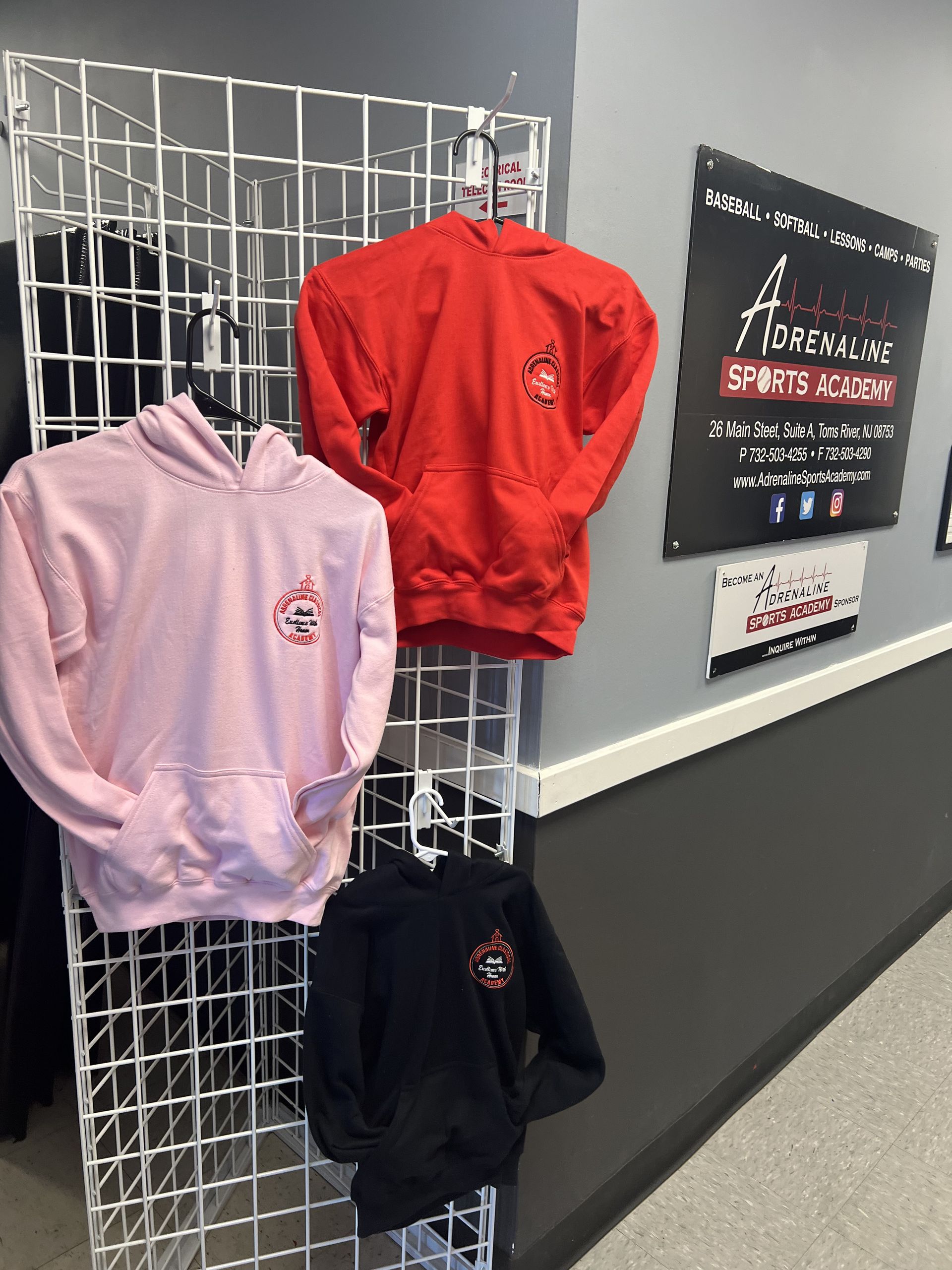 Pink, red, and black hoodies hanging on a wire display rack in a sports center.