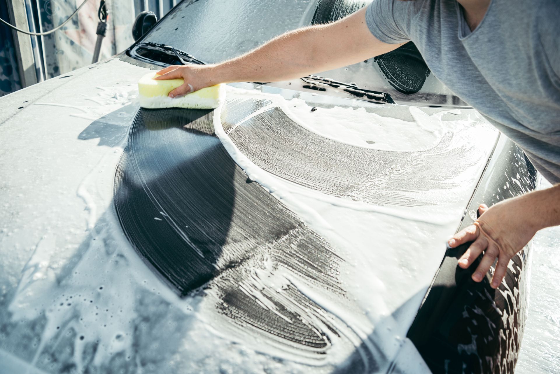 Man washing a car windshield with a high-pressure hose at a car wash.