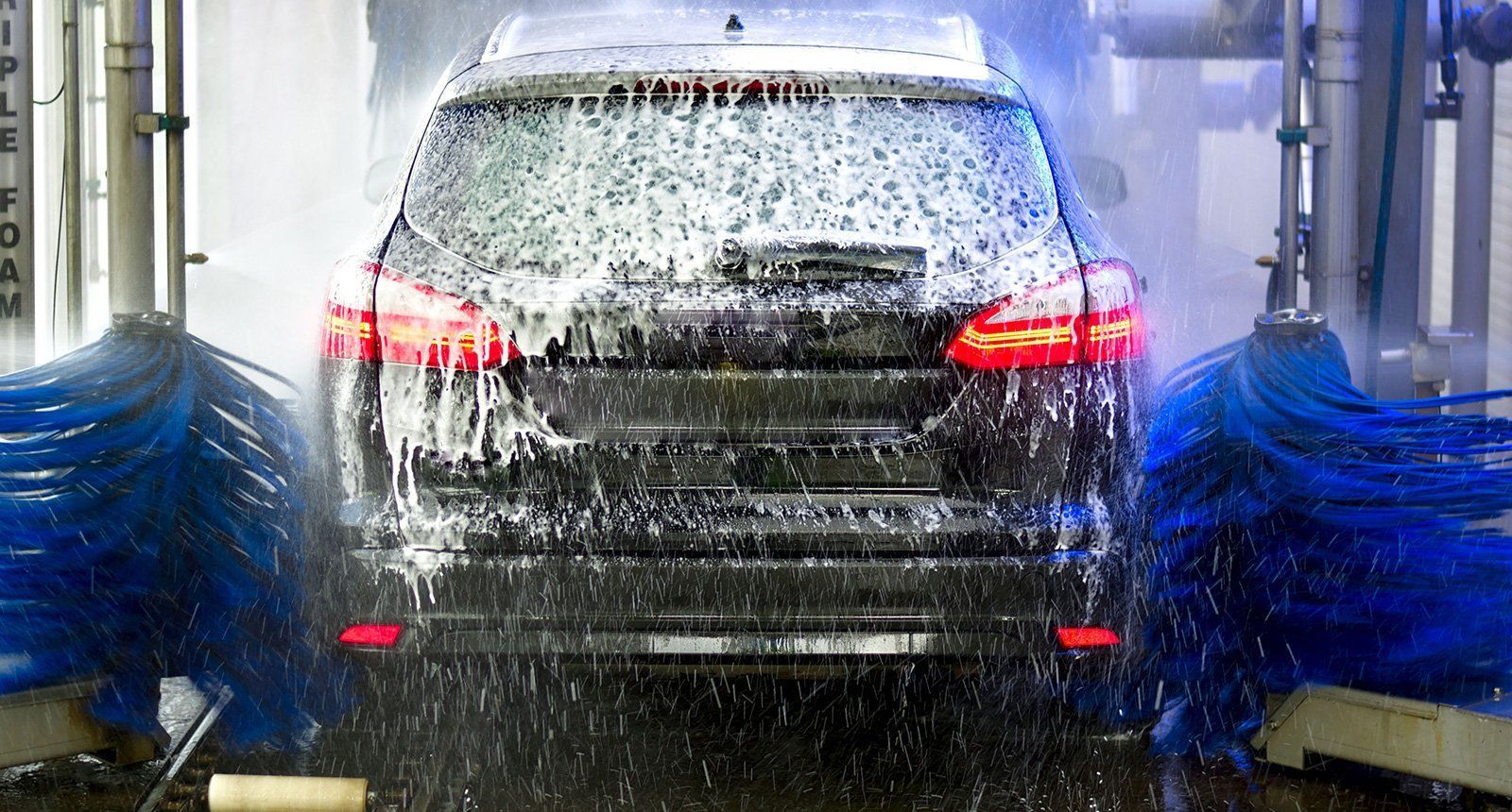 Black SUV in a car wash, covered in suds, blue brushes washing it.